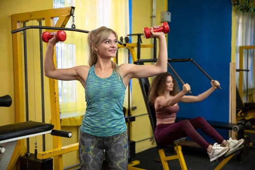 Two female friends exercising together and using sports equipment at the gym