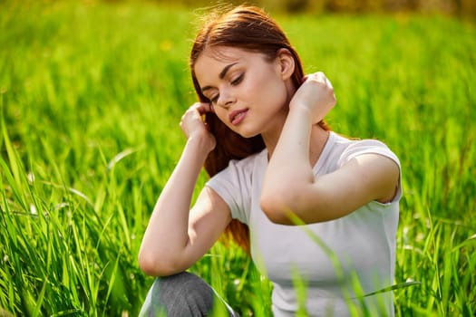 portrait of a pensive redhead woman sitting in the grass at sunset