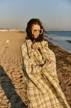 a beautiful woman wrapped in a plaid stands on the seashore against the backdrop of sunset