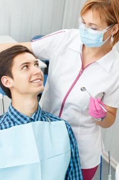 Female dentist and young man in dentist office. Handsome young man is having dental check up in dental office