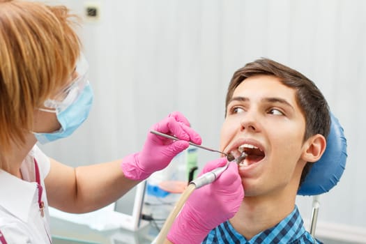 Female dentist is treating a patient tooth in dental office with focus on patient mouth