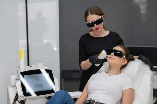 A woman on a couch in goggles undergoing a photorejuvenation procedure. Hardware cosmetology.