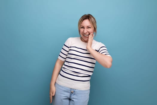 optimistic photo of a positive cheerful blond girl in a striped sweater on a blue background with copy space