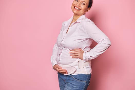 Close-up smiling pregnant woman wearing a comfortable orthopedic bandage to reduce pain in the back during pregnancy