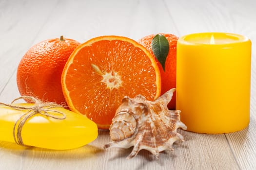 Cut orange with two whole oranges, soap, sea shell and burning candle on wooden desk. Spa products and accessories