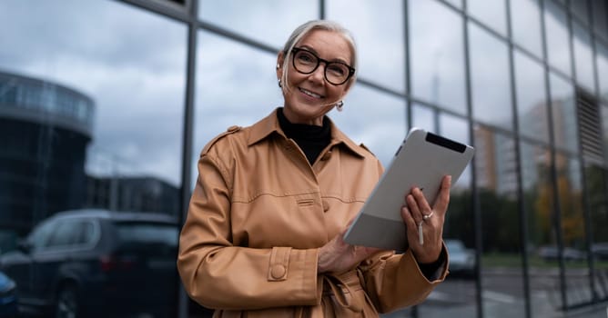 elderly stylish woman with a tablet on the background of a business center, woman leader in business concept