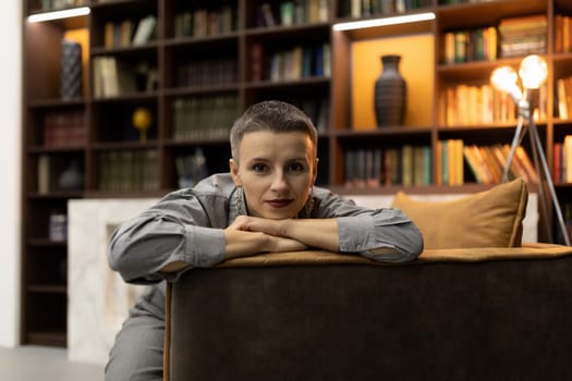 confident woman sitting in an armchair against the backdrop of a cozy home library