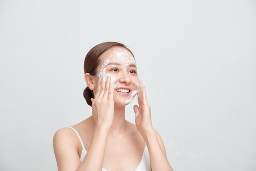Happy attractive young Asian woman applying foaming cleanser on her face over white background.