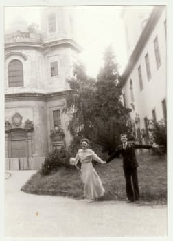 Vintage photo shows young newlyweds - bridal couple in front of church. Retro black and white photography. Circa 1980.
