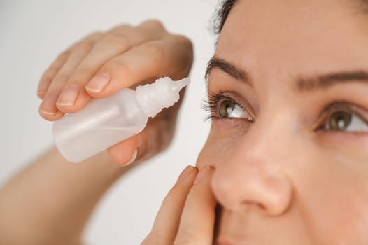 Caucasian woman dripping moisturizing drops into her eyes.