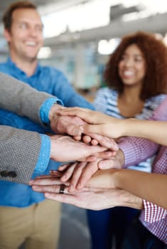 Getting it done with teamwork. a group of smiling coworkers standing hand in hand in a huddle in an office.