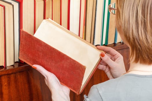 Woman with glasses is holding an old book nex to a bookshelf
