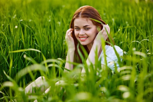 beautiful, elegant woman with red hair sits in tall green grass and smiles