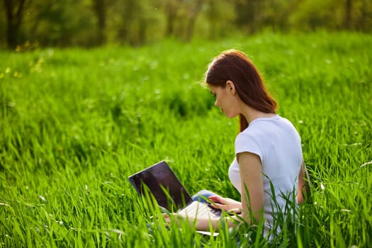 a woman with laptop sitting in a city park on the lawn on a hot summer day