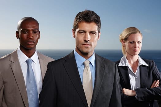 Our team is number 1. A portrait of three serious businesspeople standing with the ocean in the background.