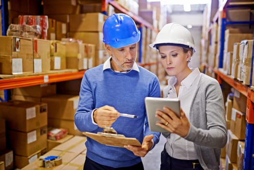 Comparing order stats. a man and woman inspecting inventory in a large distribution warehouse.