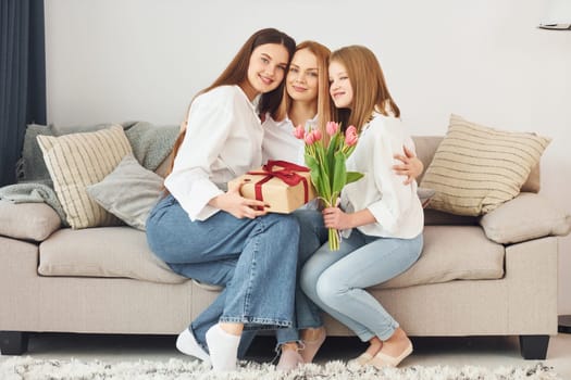 Making surprise with flowers. Young mother with her two daughters at home at daytime