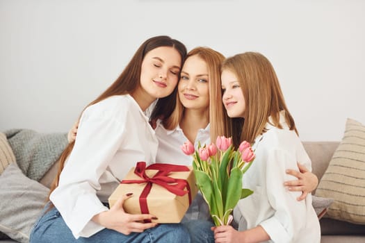 Making surprise with flowers. Young mother with her two daughters at home at daytime