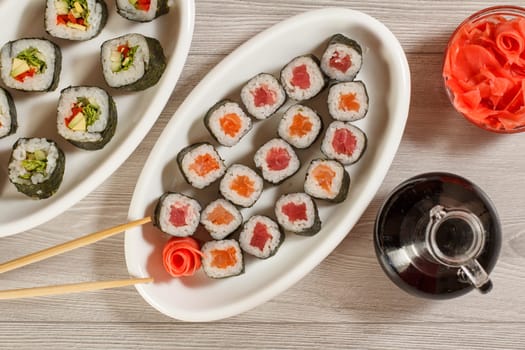 Sushi rolls with rice on plate, chopsticks and glass bottle with soy sauce