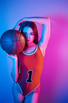 In basketball uniform. Fashionable young woman standing in the studio with neon light