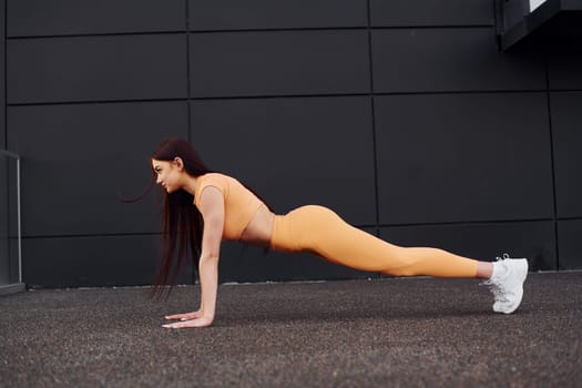 Doing push ups. Young woman in sportswear have fitness session outdoors
