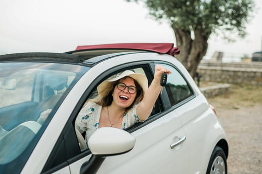 Travelling woman holding keys to new car and smiling at camera - ownership and purchase automobile concept