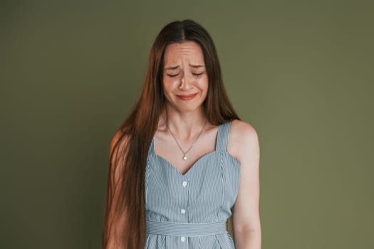 Young woman in casual clothes is crying while standing indoors in the studio