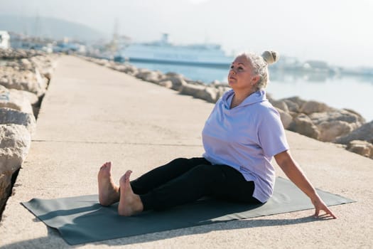 Mature old woman with dreadlocks practicing yoga and tai chi outdoors by the sea - wellbeing and wellness