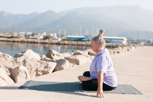 Mature old woman with dreadlocks practicing yoga and tai chi outdoors by the sea - wellbeing and wellness