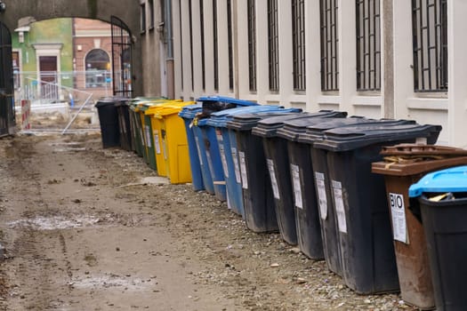 Rows of garbage cans of different colors in an alley in the city center, near a construction site