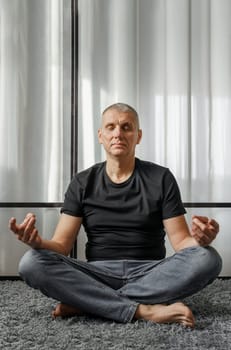 A man meditates in the lotus position on a yoga mat during a break from work.