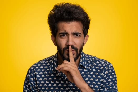 Young indian man presses finger to lips makes silence gesture sign do not tells secret, stop gossip