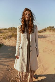 a red-haired woman stands in the desert in light clothes in windy weather looking at the camera. High quality photo