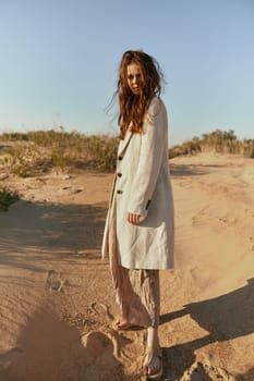 a red-haired woman stands in the desert in light clothes in windy weather looking at the camera. High quality photo