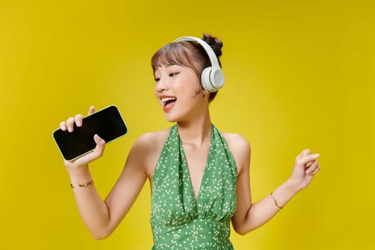 Happy young woman in headphones listening to music on vivid yellow background