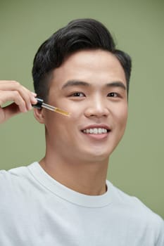 Young man applying organic essential serum on face with pipette