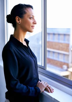 Leadership is a tough but rewarding road. a pensive businesswoman looking out of an office window.