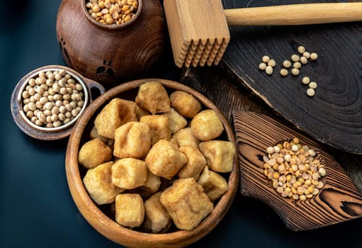 Brown fried tofu puffs or Deep Fried Tofu in wooden bowl and grains (soybeans) with dark background.