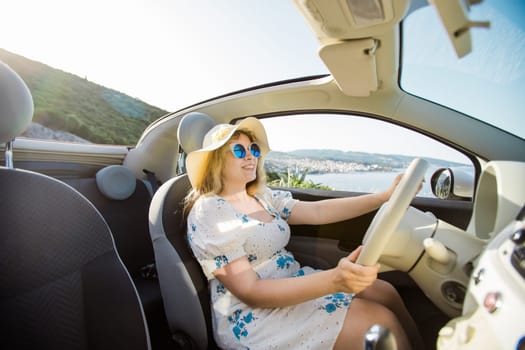 Smiling woman wearing hat and sunglasses enjoying her summer road trip in cabrio car. Freedom and tourism vacation. travel trip and summer holidays