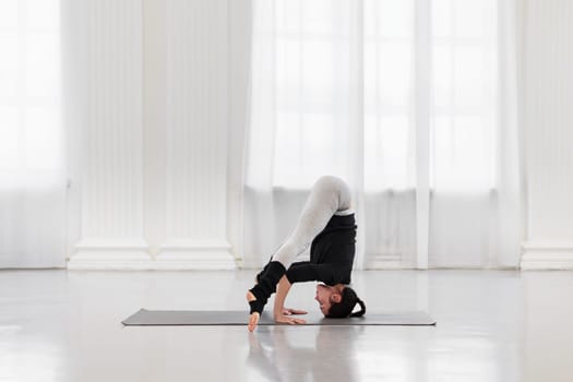 Slim young woman doing headstand preparation during yoga class in bright gym. Concept of relieving tension in the body, relaxation, improving metabolism, balance and concentration