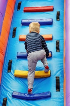 Brave little boy child climbs the stairs of a multi-colored slide in the attraction park