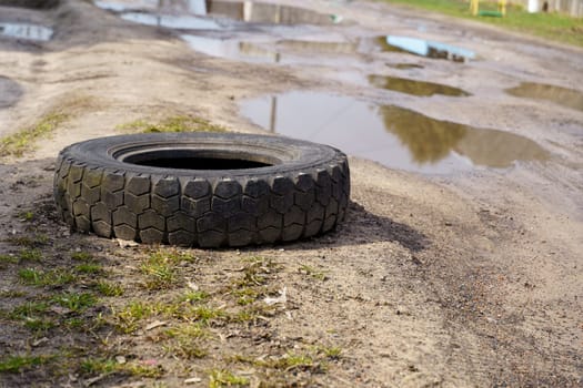 a black car tire lies on the side of an old dirt road with pits and puddles
