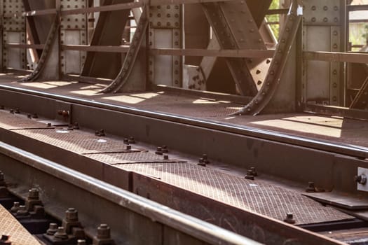 Rail bridge, detail on tracks, steel plates, large nuts and bolts lit by sun.