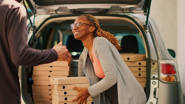 Female courier delivering pizza boxes stack from car trunk