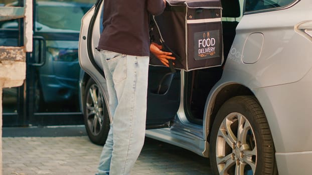 Restaurant employee taking backpack out of car to deliver fastfood