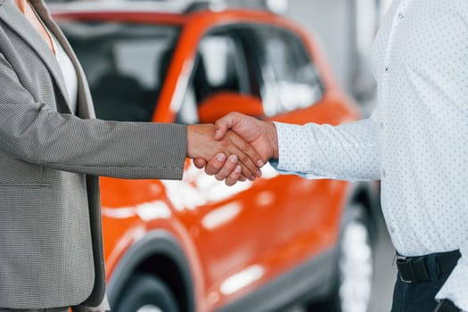 Doing handshake. Man in formal wear helping customer with choice of the automobile