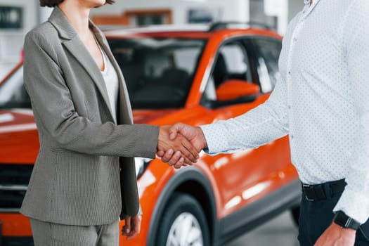 Doing handshake. Man in formal wear helping customer with choice of the automobile