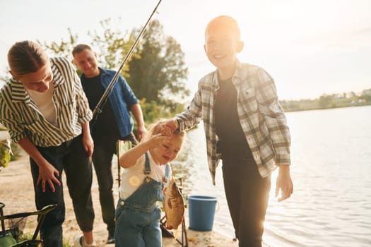 Rural scene. Father and mother with son and daughter on fishing together outdoors at summertime.
