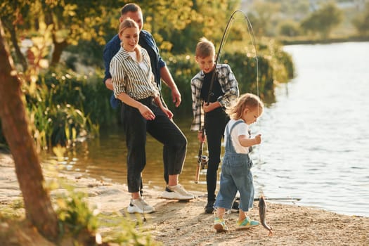Middle sized lake. Father and mother with son and daughter on fishing together outdoors at summertime.