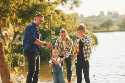 At summertime. Father and mother with son and daughter on fishing together outdoors.
